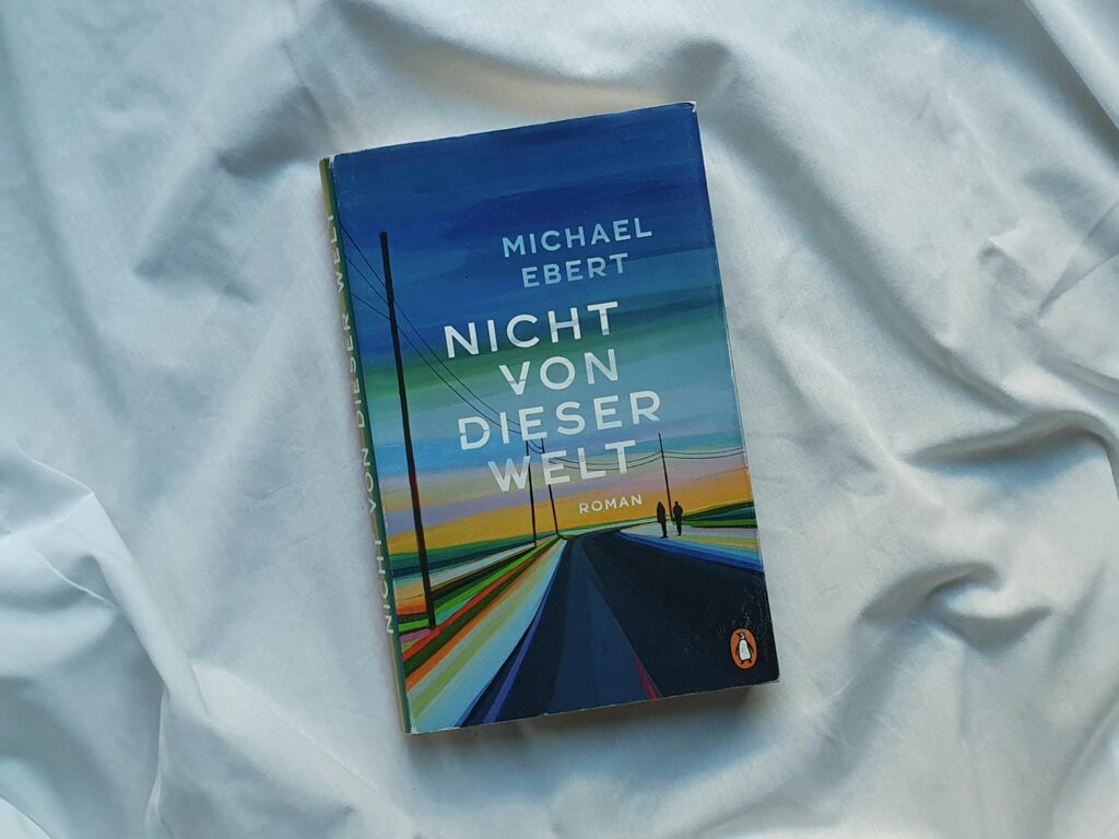 Das Buch "Nicht von dieser Welt" auf weißem Grund. Das Cover zeigt eine Straße, auf der zwei Gestalten laufen.